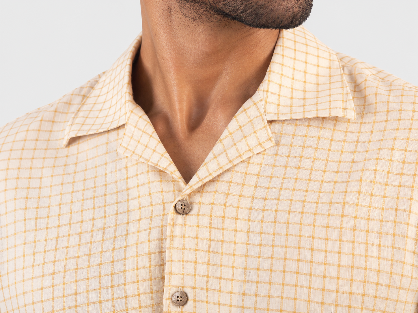 Cream and golden checked shirt with turquoise floral embroidery, button front and short embroidered sleeves Close-up of the open collar and button front on the cream and golden checked shirt Turquoise floral embroidery beside the button front on the checked shirt Short sleeve finished with turquoise leaf embroidery along the border[1]